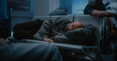 Kalabalık Uluslararası Havalimanı Terminali: Yorgun Adam Sırt çantasında Uyuyor Gece Havalimanı 'nın Yatılı Salonunda. Çeşitli İnsanlar ve Yolcular Gecikmiş Uçak Uçuşunu Bekliyor.