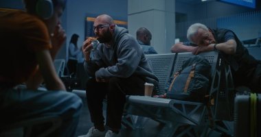 Kalabalık Uluslararası Havalimanı Terminali: Adam Fast Food Yiyiyor Yatılı Havayolu Merkezinde Geceleyin oturuyor. Yorgun Yolcular ve Turistler Koltuklarda Uyuyor, Gecikmiş Uçak Uçuşunu Bekliyor.