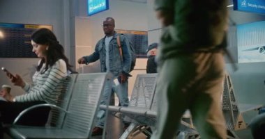 Kalabalık Uluslararası Havaalanı Terminali: Yolcular ve Yolcular Biniş Salonu 'nda. Bavullu Afro-Amerikan Adam Akıllı Telefon kullanarak uçağın kalkmasını bekliyor..