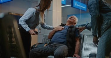 Kalabalık Uluslararası Havaalanı Terminali: Yaşlı Adam Kalp krizi geçiriyor, Acılı Göğsü Sıkışan Hava Yolları Merkezinde Oturuyor. Çeşitli İnsanlar ve Havalimanı Personeli Yaşlı Yolculara Yardım Ediyor.