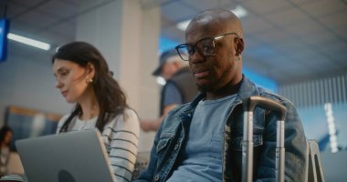 Kalabalık Uluslararası Havaalanı Terminali: Laptop 'ta çalışan Afrikalı Amerikalı Adam, Çevrimiçi Video Sohbeti Var. Çeşitli İnsanlar ve Yolcular, Havayolu Merkezinin Kalkış Salonu 'nda, Uçuşu Bekliyorlar..