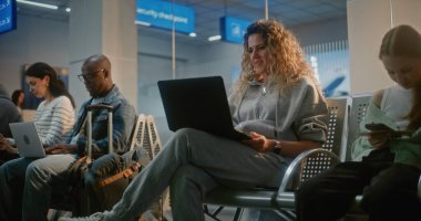 Kalabalık Uluslararası Havaalanı Terminali: Laptop 'ta Çalışan, Çevrimiçi Görüntü Arayan Kadın. Çeşitli İnsanlar, Dijital Aygıtları kullanarak, Hava Yolları Merkezi 'nin Yatılı Salonunda oturmuş, Uçak Uçuşunu bekliyor..