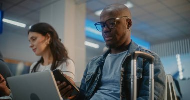 Kalabalık Uluslararası Havalimanı Terminali: Laptop 'ta Uzaktan Çalışan Afrikalı Amerikalı Girişimci, Telefonu Kullanıyor. Uçağı bekleyen çeşitli yolcular, havayolu merkezinin biniş salonunda oturuyorlar..