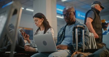 Kalabalık Uluslararası Havaalanı Terminali: Laptop 'ta Uzaktan Çalışan Afrikalı Amerikalı Adam. Yolcular, Dijital Gadget kullanarak, Uçak İndirme Merkezi Biniş Salonunda, Uçak Uçuşunu Bekliyor..