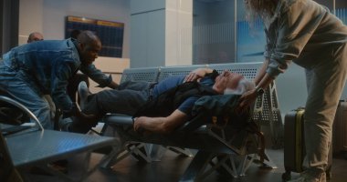 Kalabalık Uluslararası Havalimanı Terminali: Yaşlı Adam Kalp krizi geçiriyor, Infarction in Inarding Lounge of Airline Hub. Kıdemli Yolcuya Yardım Eden Çeşitli İnsanlar, Havaalanı İşçisi Tıbbi Yardım Çağrısı.