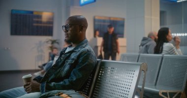 Kalabalık Uluslararası Havaalanı Terminali: Afro-Amerikan Genç Adam Oturuyor, Uçak Uçuşunu Bekliyor, Seyahate Çıkıyor. Çok Irklı İnsanlar ve Yolcular Hava Yolları Merkezinin Kalkış Salonunda.