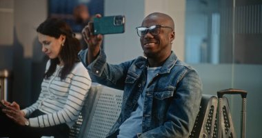 Kalabalık Uluslararası Havalimanı Terminali: Afro-Amerikan Seyahat Blogcusu Akıllı Telefon Kullanarak Seyahat Gezisinden Video İçeriği. Uçuşunu Bekleyen Çeşitli İnsanlar Hava Yolları Merkezinin Kalkış Salonunda.