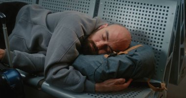 Kalabalık Uluslararası Havalimanı Terminali: Sırt çantalı Yorgun Adam 'ın Kapanışı Hava Yolları Merkezinde Koltuklarda Uyuyor. Gecikmiş Uçak Uçuşunu Bekleyen Yolcu. Turizm ve Seyahat.