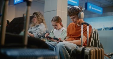 Kalabalık Uluslararası Havaalanı Terminali: Erkek ve Kız, Genç Kardeşler Akıllı Telefon Kullanıyor, Atıştırmalık yiyor, Seyahat İçin Uçuşu Bekliyor. Farklı Yolcular Hava Yolları Merkezinin Kalkış Salonunda Oturuyorlar.