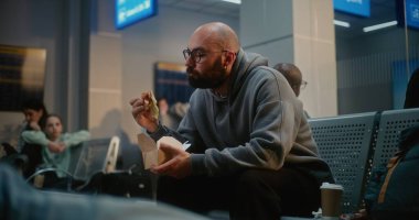 Kalabalık Uluslararası Havaalanı Terminali: Fast Food Yiyen Adam Havayolu Merkezinin Gidiş Salonunda Oturuyor. Çeşitli Yolcular ve Gezginler Gecikmiş Uçak Uçuşunu Bekliyor, Tatile Çıkıyor.