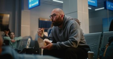 Kalabalık Uluslararası Havaalanı Terminali: Fast Food Yiyen Adam Havayolu Merkezinin Gidiş Salonunda Oturuyor. Çeşitli Yolcular ve Gezginler Gecikmiş Uçak Uçuşunu Bekliyor, Tatile Çıkıyor.