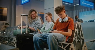 Kalabalık Havaalanı Terminali: İki Genç Çocuklu Kadın ve Pasaport Kontrolünden Sonra Kalkış Salonunda Oturan Kadın, Uçuşu Bekliyor. Arka planda, Güvenlik Kontrolünde Bekleyen İnsanların Kuyruğu.