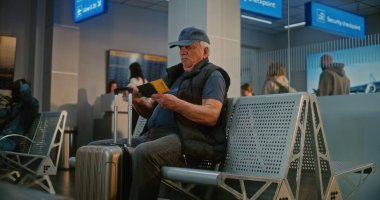 Kalabalık Havaalanı Terminali: Bavulu ve pasaportu olan yaşlı adam güvenlik kontrolünden sonra kalkış salonunda oturuyor, uçak biletini kontrol ediyor, uçuş için bekliyor. Belge Kontrolünde Duran İnsanların Kuyruğu.