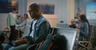 Kalabalık Uluslararası Havaalanı Terminali: Laptop kullanan Afrikalı Amerikalı Adam, Küçük Bebekle Oturan Kadın. Çeşitli Gezginler, Yolcular, Uçak Kalkış Salonunda Uçak Uçuşunu Bekliyor.