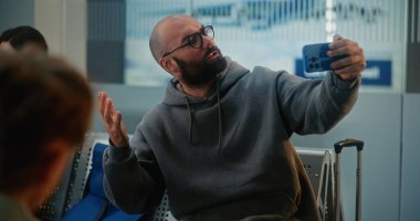 Kalabalık Uluslararası Havaalanı Terminali: Popüler Seyahat Blogcusu Akıllı Telefon Kullanarak Seyahat Video İçeriği, Uçuşu Bekleme. Havayolu Merkezinin Ayrılış Salonunda Farklı İnsanlar Oturuyor.