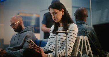 Kalabalık Uluslararası Havaalanı Terminali: Akıllı Telefon Kullanan, Kaydıran ya da Uzaktan Çalışan, Uçuşu Bekleyen Kadın. Farklı Yolcular Dijital Gadget 'larla Havayolu İnbotu' nun Yatılı Salonunda Oturuyorlar.