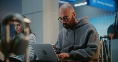 Kalabalık Uluslararası Havaalanı Terminali: İnternette Çalışan Girişimci, E-İş Yapıyor, Uçuşu Bekliyor. Dijital Aygıtları kullanarak, Hava Yolları Merkezinin Ayrılış Salonunda Oturan Çeşitli İnsanlar.