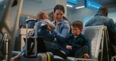 Kalabalık Uluslararası Havaalanı Terminali: Uçak Uçuşunu Bekleyen İki Küçük Çocuğu Olan Anne, Küçük Çocuk Dijital Tablet 'te Çizgi Film İzliyor. Hava Yolları Merkezinin Ayrılış Salonundaki Çeşitli Yolcular.