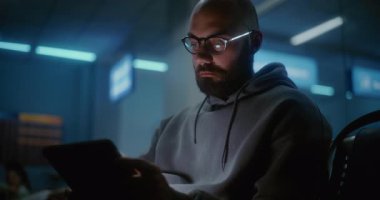 Kalabalık Uluslararası Havaalanı Terminali: Yorgun ve Uykucu Adam Tablet Bilgisayar Kullanıyor, Gece Havalimanı 'nın Kalkış Salonu' nda Oturuyor. Çeşitli Yolcular ve Gezginler Gecikmeli Uçuşu Bekliyor.