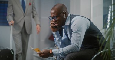 Havaalanı Terminali: Afro-Amerikan İşadamı Gecikmeli Uçuş Konuşması ve Smartphone 'da Bağrışma Hakkında Kızgın, Uçak Bileti Tutuyor. Girişimci Ayrılış Salonunda Oturuyor, İş Gezisine Gidiyor.