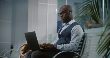 Uluslararası Havalimanı Terminali: Laptop ve Smartphone kullanan Afro-Amerikan İşadamı, İçen Kahve, İnternette Çalışan. Girişimci Ayrılış Salonunda Uçuş Bekliyor. Dolly shot, orta boy.