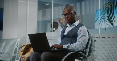 Uluslararası Havalimanı Terminali: Laptop ve Smartphone kullanan Afro-Amerikan İşadamı, İçen Kahve, İnternette Çalışan. Girişimci Ayrılış Salonunda Uçuş Bekliyor. Dolly shot, orta boy.