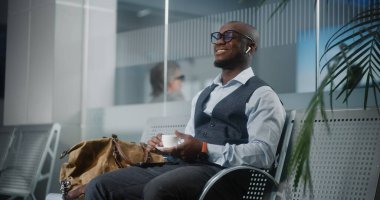 Havaalanı Terminali: Akıllı Telefon Kullanımı ve İçme Kahvesi ile Başarılı Girişimci. Afrika kökenli Amerikalı iş adamı, kalkış salonunda uçak bekliyor, iş gezisine çıkıyor. Yavaş Hareket, Orta Çekim.