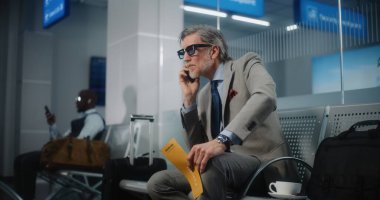 Havaalanı Terminali: Ciddi İşadamı Smartphone konuşuyor, Uçuş bilgilerini kontrol ediyor, uçak biletini tutuyor. Başarılı Olgun Adam Ayrılış Salonu 'nda oturuyor, iş gezisine çıkıyor. Yavaş Hareket.