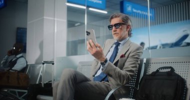 Havaalanı Terminali: Başarılı İşadamı Smartphone 'da İş Ortağıyla Konuşuyor, Video Call, Oturma Salonu. Girişimci Uçak Uçuşunu Bekliyor, Seyahate Çıkıyor. Yavaş Hareket.