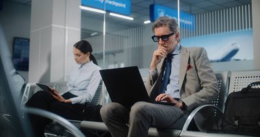 Uluslararası Havalimanı Terminali 'ndeki VIP Gidiş Salonu: Olgun İşadamı Laptop Kullanıyor, E-posta Gönderiyor. Uçuşu Bekleyen Dijital Aygıtlarla çalışan çeşitli iş adamları. Doli Vuruşu.