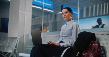 Havaalanı Terminali: Başarılı iş kadını Laptop kullanıyor, e-iş yapıyor ya da uzaktan çalışıyor, kameraya bakıyor. Girişimci iş seyahatine çıkıyor, Kalkış Salonunda Uçuşu Bekliyor. Doli Vuruşu.