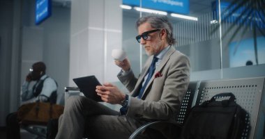 Havaalanı Terminali: Dijital Tablet ve İçme Kahvesi kullanan başarılı girişimci, e-iş yapıyor. İşadamı Uzaktan Çalışmalar Çevrimiçi Ayrılış Salonunda Uçuş Bekliyor. Yavaş Hareket, Orta Çekim.