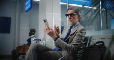 Havaalanı Terminali: Başarılı Girişimci Akıllı Telefondan Yatırımcıyla Konuşuyor, Video Sohbeti. İş adamı uçak uçuşunu bekleme salonunda bekliyor, iş seyahatine çıkıyor. Yavaş Hareket, Orta Çekim