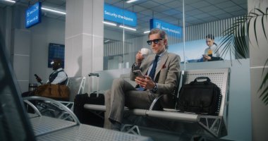 Uluslararası Havalimanı Terminali: Başarılı Adam Kalkış Salonunda Bavul, Cep Telefonu Kullanımı ve İçme Kahvesi ile Oturuyor. Olgun iş adamı uçuşu bekliyor, iş gezisine çıkıyor. Doli Vuruşu.