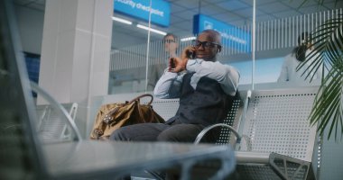 Uluslararası Havalimanı Terminali: Afrikalı Amerikalı İşadamı Cep telefonuyla İş Ortağıyla Konuşuyor. Başarılı Girişimci, Hava Yolları Merkezinin Kalkış Salonunda Uçuş Bekliyor, Seyahate Çıkıyor.