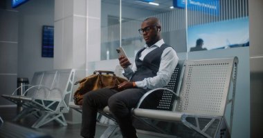 Uluslararası Havaalanı Terminali: Çantalı Afro-Amerikan İşadamı Akıllı Telefon Kullanıyor, İş Gezisine Gidiyor. Girişimci Uçuşu Bekliyor, Hava Yolları Merkezinin Kalkış Salonunda Oturuyor. Yavaş Hareket