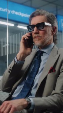 Havaalanı Terminali: Ciddi İşadamı İş Ortağıyla Cep Telefonu Konuşuyor, Ayrılış Salonunda Oturuyor. Başarılı Adam Uçak Uçuşunu Bekliyor, Seyahate Çıkıyor. Dolly Shot. Dikey Çekim.