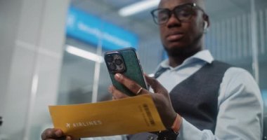 Havaalanı Terminali: Afrikalı Amerikalı Adam Akıllı Telefon kullanarak uçak biletini tarıyor, bilgileri kontrol ediyor. VIP Ayrılış Salonunda Uçağı Bekleyen İşadamı. E-Bilet Teknolojisi. Rack Odağını Kapat