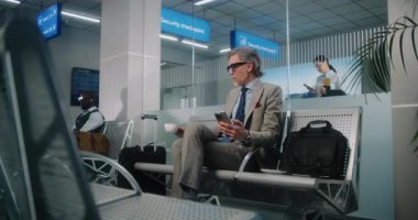 Uluslararası Havalimanı Terminali: Başarılı Adam Kalkış Salonunda Bavul, Cep Telefonu Kullanımı ve İçme Kahvesi ile Oturuyor. Olgun iş adamı uçuşu bekliyor, iş gezisine çıkıyor. Doli Vuruşu.