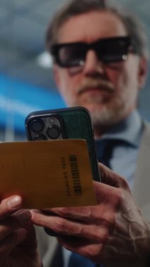 Havaalanı Terminali: Başarılı İşadamı Tarayıcı Uçuş Bilgilerini Kontrol ederek Akıllı Telefon kullanarak Uçuş Geçidi. Girişimci VIP Ayrılış Salonunda oturuyor. E-Bilet Teknolojisi. Dikey Görüntüyü Kapat