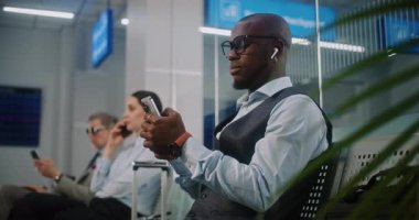 Uluslararası Havalimanı Terminali 'ndeki VIP Gidiş Salonu: Akıllı Telefon Kullanan Afrikalı Amerikalı İşadamı, E-İş Yapıyor. Uçuşu Bekleyen Dijital Gadget 'larla çalışan çok ırklı iş adamları.