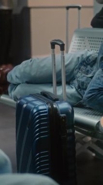 Kalabalık Uluslararası Havaalanı Terminali: Bavullu yorgun Afrikalı Amerikalı Adam ve Sırt Çantası Gidiş Salonunda Uyuyor. Çeşitli yolcular rötarlı uçuş bekliyor. Dikey Çekim.