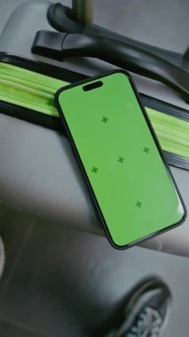 Kalabalık Havaalanı Terminali: Yeşil Kroma Anahtarlı Akıllı Telefon Bavulun Üzerinde Uzanıyor. İş Dünyası Reklamcılığı ve Sosyal Medya İçeriği için Video Şablonu. El bilgisayarı. Dikey Çekim.