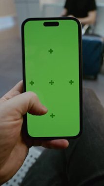 Havaalanı Terminali: POV Adam Yeşil Krom Ekran Modifiye ile Kalkış Salonunda Oturuyor, Akıllı Telefon Kaydırıyor. Sosyal Medya İçeriği için Yer Tutucu ile Görüntü Şablonu. Birinci şahıs. Dikey Çekim.