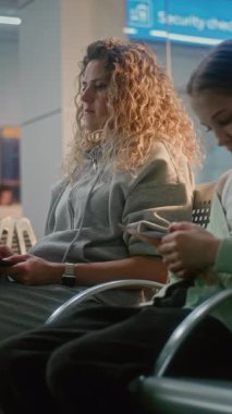 Kalabalık Uluslararası Havaalanı Terminali: Laptop 'ta Çalışan Kadın, E-posta Gönderiyor. Çeşitli İnsanlar, Biniş Salonunda oturan Yolcular, Uçak Uçuşunu Bekleyen, Telefonları Kullanan. Dikey Çekim.