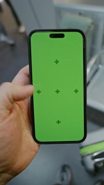 Kalabalık Havaalanı Terminali: Man Standing in Airline Hub Lounge, Holding Mobile Phone with Green Chroma Key Moplay Mock Up. İş Reklamcılığı için video şablonu. Birinci Şahıs Görünümü. Dikey Çekim.