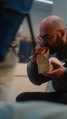 Kalabalık Uluslararası Havaalanı Terminali: Fast Food Yiyen Adam Gidiş Salonunda Oturuyor. Çeşitli Yolcular ve Gezginler Gecikmiş Uçak Uçuşunu Bekliyor, Tatil Gezilerine Gidiyor. Dikey Çekim.