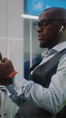 Havaalanı Terminali 'ndeki VIP Gidiş Salonu: Afrika kökenli Amerikalı İşadamı Akıllı Telefon Kullanıyor, E-İş Yapıyor. Uçuşu Bekleyen Dijital Gadget 'larla çalışan çok ırklı iş adamları. Dikey Çekim.