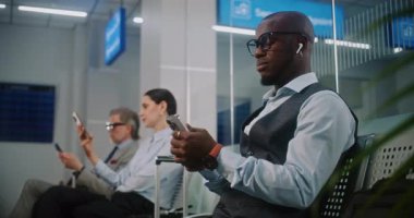 Uluslararası Havalimanı Terminali 'ndeki VIP Gidiş Salonu: Afrika kökenli Amerikalı İşadamı Smartphone' da çalışıyor. Uçak Uçuşunu Bekleyen Dijital Aygıtları kullanan Çeşitli İş Adamları. Doli Vuruşu.
