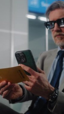 Havaalanı Terminali: Başarılı İşadamı Tarayıcı Uçuş Bilgilerini Kontrol ederek Akıllı Telefon kullanarak Uçuş Geçidi. Olgun Girişimci VIP Ayrılış Salonu 'nda oturuyor. E-Bilet Teknolojisi. Dikey Çekim.